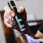Person holding a black flashlight emitting a blue light, with a blurred background.