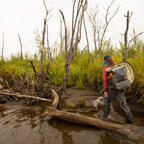 Fishing angler with a gray Fishpond Wind River Roll-Top Backpack with orange straps and zipper closure.