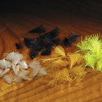 A collection of various sized Hareline CDC Oiler Puffs feathers arranged on a wooden surface.