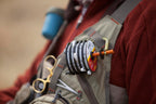 An image of the Fishpond Headgate Tippet Holder, which is designed to dispense fishing line, featuring a spool with line, a cutting blade, and a spring-loaded mechanism.