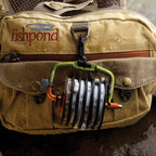 An image of the Fishpond Headgate Tippet Holder, which is designed to dispense fishing line, featuring a spool with line, a cutting blade, and a spring-loaded mechanism.