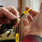 Close-up of hands using a Loon hackle plier tool with a blurred background