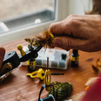 Person preparing a fly fishing lure with Loon Ergo Hair Packer on a wooden surface.