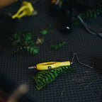 Yellow Loon whip finisher tool on a textured black surface with green feathers. 
