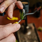Yellow Loon whip finisher tool with a metal hook on a fly tying desk background
