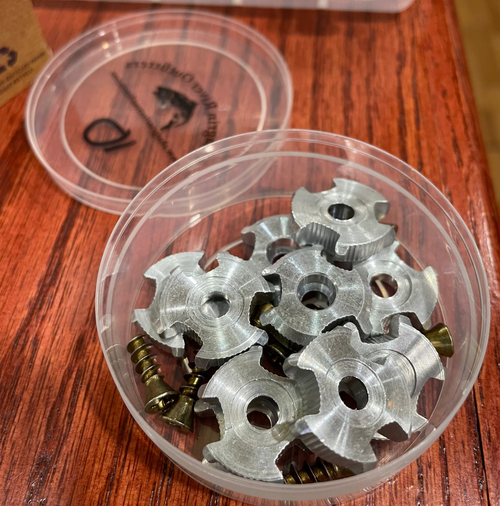 A clear plastic box containing aluminum star wading boot cleats, placed on a wooden surface.