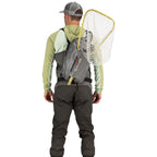 Person wearing waders and a Gray Simms Dry Creek Z Sling Pack with a fishing net on a white background
