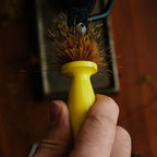 Yellow Loon Ergo Hair Packer with bristles being held by a hand against a blurred background