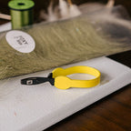 Yellow Loon hackle pliers with a black clip on fly tying desk background 