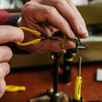 Person using yellow Loon hackle pliers to wrap a green feather on a fly fishing hook.