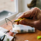 Yellow Loon whip finisher tool with a metal hook on a fly tying desk background . 