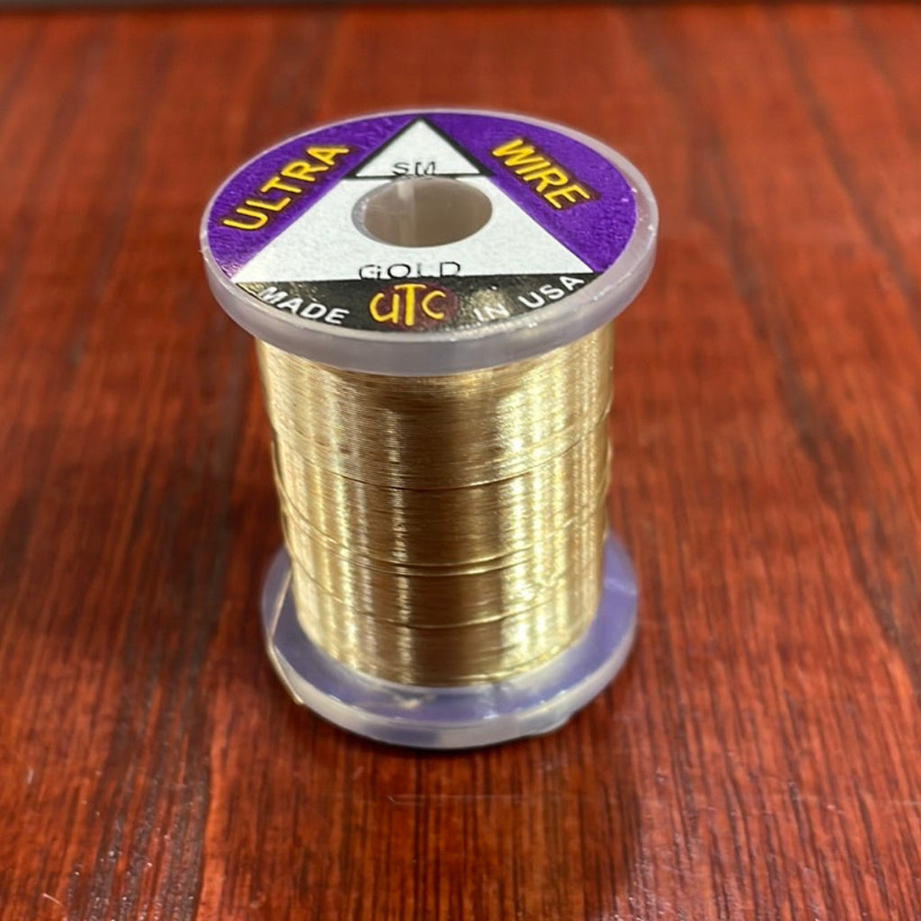 Spool of gold Wapsi Ultra Wire UTC with a purple label on a wooden surface