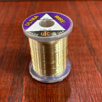 Spool of gold Wapsi Ultra Wire UTC with a purple label on a wooden surface