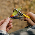 Person holding a colorful fly fishing lure with a Loon comb against a blurred natural background