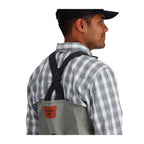 Person wearing Simms Men's Freestone Stockingfoot Waders, featuring gray upper and lower layers with black suspenders and red adjustment straps.