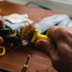 Person using a fly fishing tool with a brush on a wooden surface