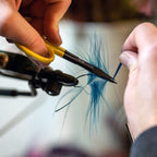 Person using Loon Ergo Precision Tip Scissors to cut blue feathers with a blurred background