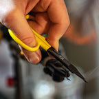 Hand holding yellow-handled Loon Ergo Precision Tip Scissors cutting a wire with a blurred background