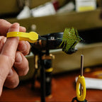 Person using yellow Loon hackle pliers to wrap a green feather on a fly fishing hook.