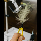 Fishing fly being worked on with a Loon hackle plier and a bottle of glue.
