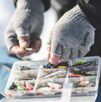 Person holding a tackle box with fishing lures and hooks.