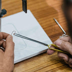 Person using a Loon Ergo D-Loop Tweezer on a piece of paper with a wooden surface underneath