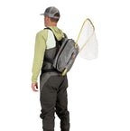 Man wearing waders and a Gray Simms Dry Creek Z Sling Pack with a fishing net on a white background