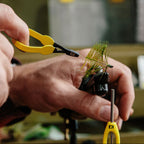 Person using yellow Loon hackle pliers to wrap a green feather on a fly fishing hook.