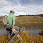 A fisherman with a Fishpond Switchback Belt System 2.0 with various pockets and straps, featuring a wader belt and a shoulder strap, in green, gray, and orange colors.