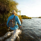 Fishing angler wearing a Fishpond Summit Sling Pack 2.0 while wading a river.
