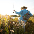Fishing angler wearing a Fishpond Summit Sling Pack 2.0 while wading a river.