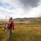 Fishing angler wearing a Fishpond Summit Sling Pack 2.0 while wading a river.