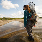 Fishing angler wearing a Fishpond Summit Sling Pack 2.0 while wading a river.