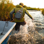 Fishing angler wearing a Fishpond Summit Sling Pack 2.0 while wading a river.