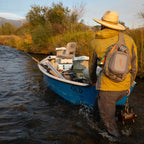 Fishing angler wearing a Fishpond Summit Sling Pack 2.0 while wading a river.