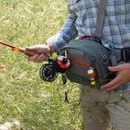 A fisherman with a Fishpond Switchback Belt System 2.0 with various pockets and straps, featuring a wader belt and a shoulder strap, in green, gray, and orange colors.